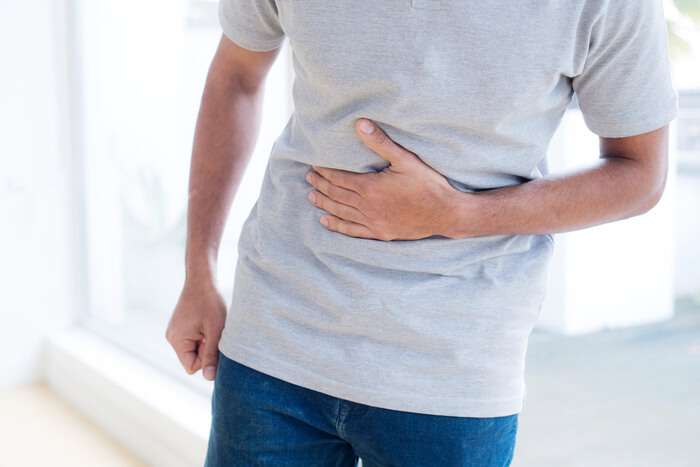 Man in t-shirt gripping midsection in discomfort.