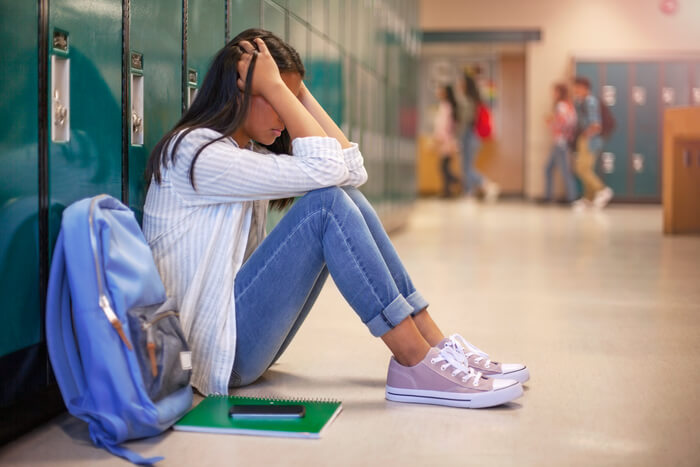 Visibly upset school girl setting in front of locker.