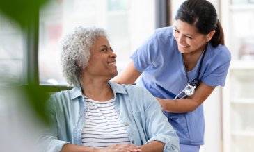 A nurse smiling at a patient in a wheelchair
