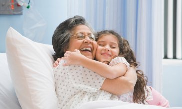 Woman in a hospital bed smiling and hugging her granddaughter