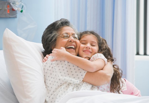 Mujer en una cama de hospital sonriendo y abrazando a su nieta