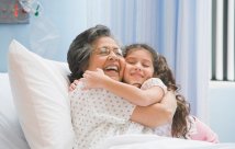 Mujer en una cama de hospital sonriendo y abrazando a su nieta