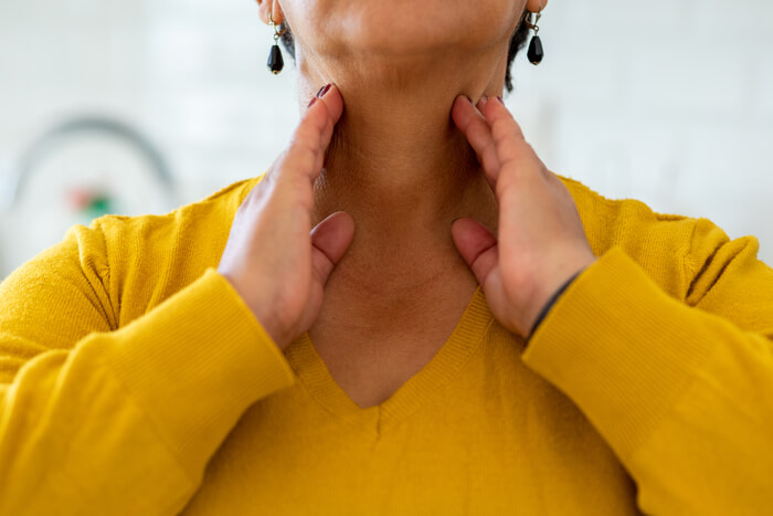 Woman in a yellow sweater with both hands on her throat.
